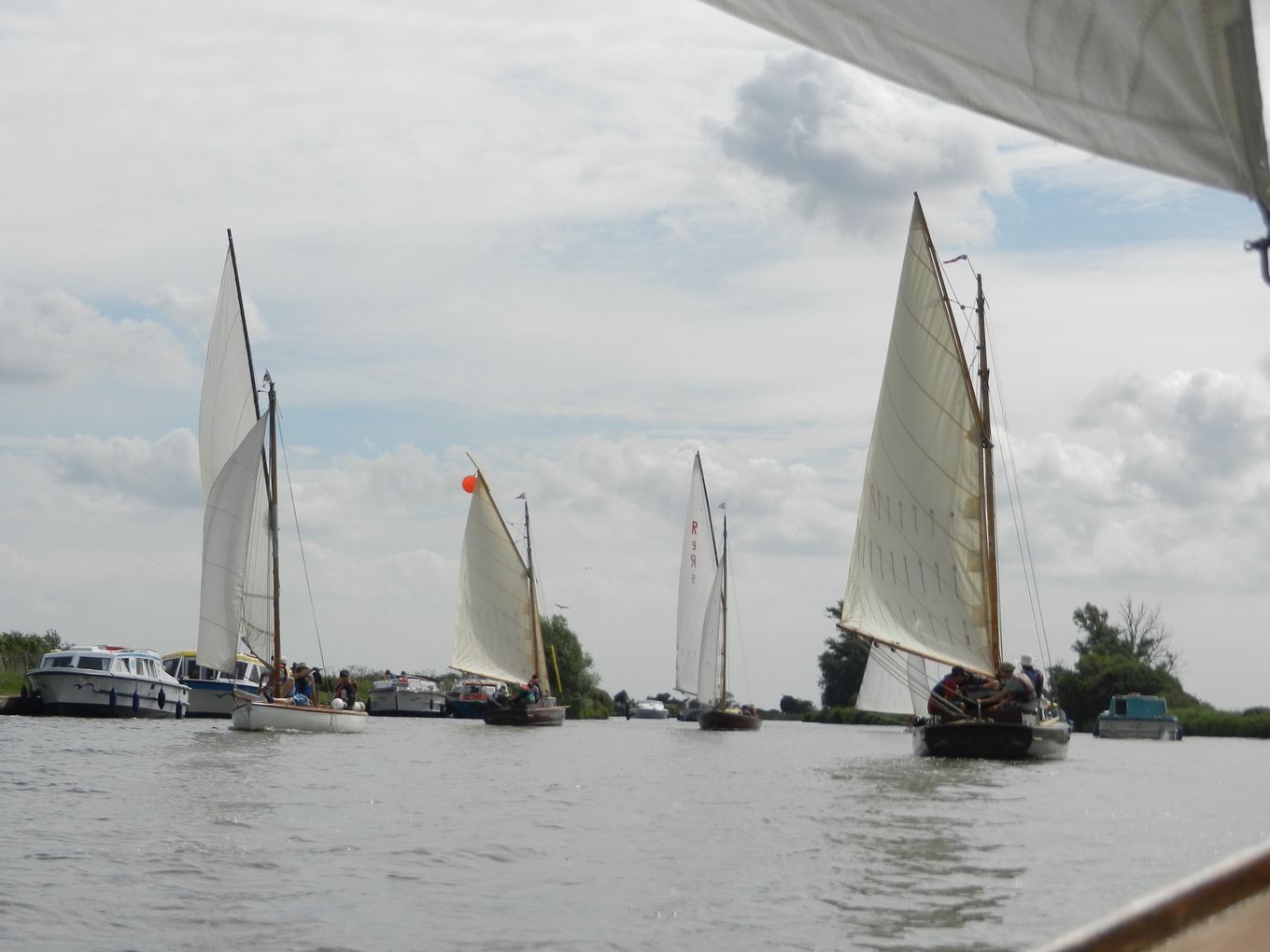 A fleet of traditional wooden boats sailing along the River Bure.